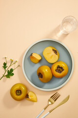 Top view of blue dish of persimmon , pork , knife , water glass in light pink background for food advertising 
