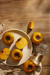 Top view of persimmon in white plate , water glass and a napkin brown wooden background for advertising 