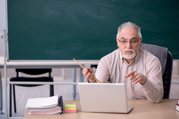 Old male teacher in front of blackboard in telestudy concept