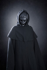 Woman ghost in hooded cloak over dark misty background