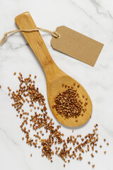 Buckwheat groats on wooden spoon and scattered on marble table.