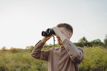 A young man looks through binoculars at a beautiful hilly landscape.The concept of hunting, travel...