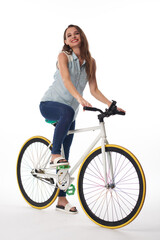 Positive active young Caucasian woman in denim outfit riding bicycle against isolated background