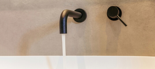 Sink basin faucet, bathroom interior detail. Open black tap with running water on white washbasin.