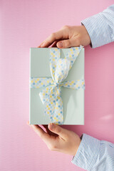 Flat lay of beautiful wrapped present box and hands holding gift box on pink