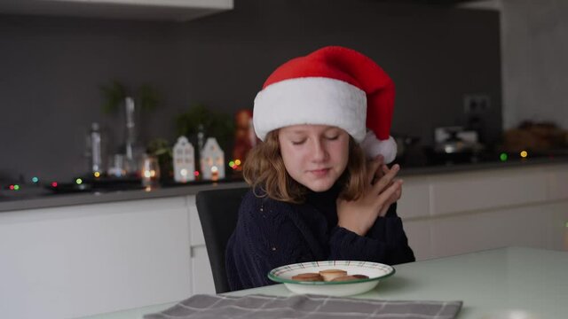  Teenage girl happy to eat typical Christmas sweets in the kitchen at home, decorated with lights and candles. Enjoying Christmas holidays of traditional food and Christmas traditions.