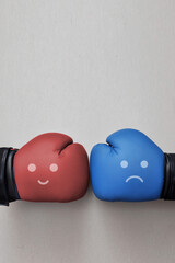 Two boxing gloves with the image of a smile and a sad face opposite each other. A symbol of a...