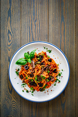 Pasta puttanesca with tomato sauce, anchovies, chili, capers and olives on wooden table
