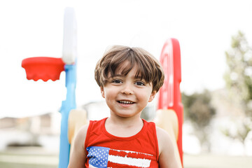 little boy playing on the backyard on a little slide with an American shirt 
