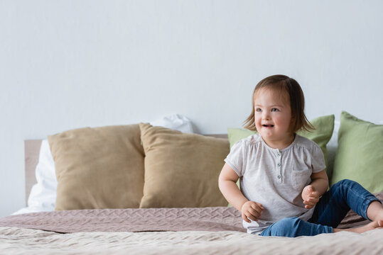 Smiling toddler girl with down syndrome sitting on bed.
