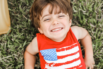 little boy playing on the backyard on a little slide with an American shirt