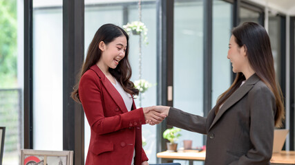 Two young Asian businesswoman shaking hands successful with a colleague in the meeting.