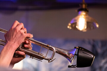 A musician playing a silver plated piston trumpet with a bucket mute during a jazz gig in a bar