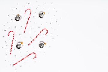 Christmas flat lay composition. Christmas candy canes, silver balls, glitter confetti stars on white background. Flat design, top view, copy space.