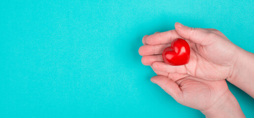 Woman is holding a red heart in her hand, blue colored background, copy space