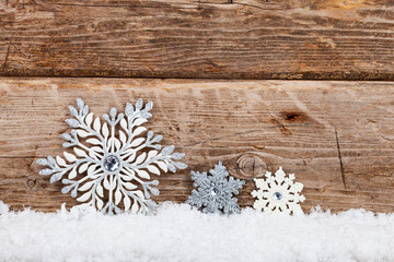 Silvery Christmas snowflakes in the snow on a wooden background.