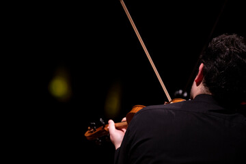 A view of a violin player dressed in concert black from behind during a solo performance