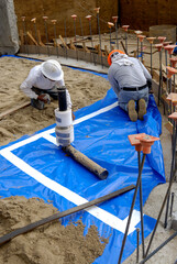 Fototapeta premium Workers installing plastic waterproof sheathing over sand before concrete