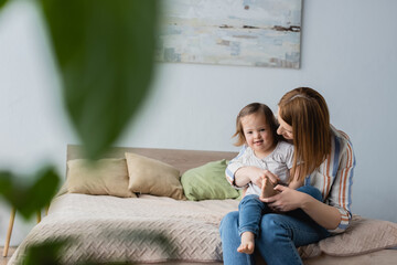 Mother embracing baby daughter with down syndrome in bedroom.