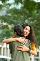 Naklejka premium Smiling adult Asian daughter with curly hair hugging mother in summer park while meeting with her
