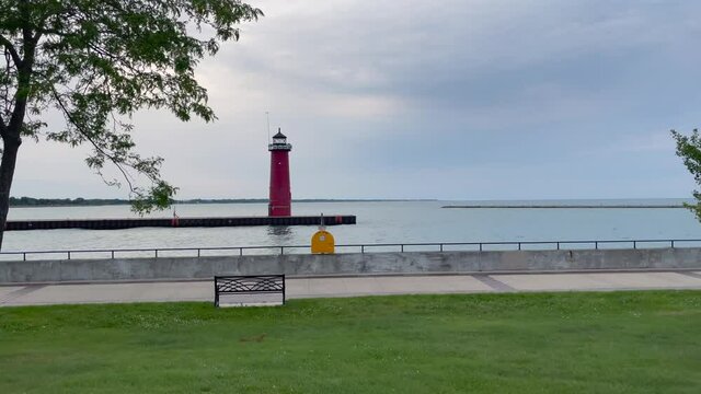 Waves over the lighthouse on Lake Michigan in Kenosha, stone wall with clouds on a calm summer day along the Wisconsin coastline with walking paths, tress, and green grass