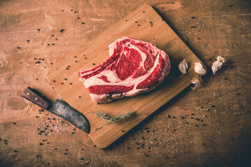 Closeup of a raw steak on a wooden board with ingredients for cooking