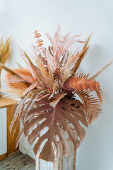 Flowers. Vase with a lush bouquet of dried flowers. Composition of palm leaves of monstrella and spikelets. Interior of the room.