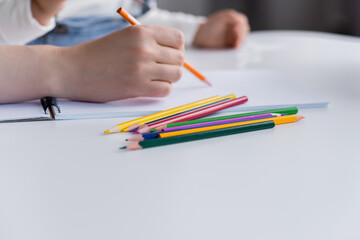 Cropped view of woman drawing near blurred child and color pencils on table.