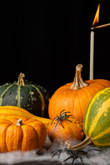 View of orange and green halloween pumpkins with burning candle with match, on table with spider web, selective focus, black background, vertical