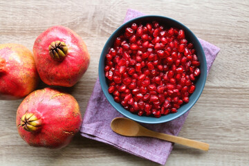 Bowl filled with pomegranate seeds and pomegranate fruit on a table. Flat lay.