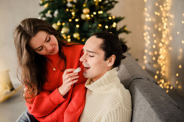 Couple in love at Christmas eve enjoy with mashmallow eating next to the christmas fir pine tree