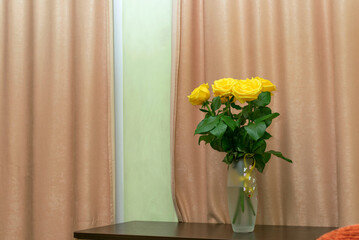 Yellow roses in a vase on the table in the room.