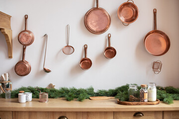 Set of saucepans hanging in kitchen. Hanging Copper kitchen utensil on the white wall. Different kind of vintage copper cookware, pans, pots and funnel on wooden kitchen. Rustic kitchen interior decor - obrazy, fototapety, plakaty