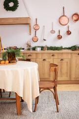  Stylish dining room in rustic style. Cozy Wooden kitchen decorated Christmas or new year. On table fir branche in vase, Xmas cookies. Interior design scandinavian kitchen with round table and chair.