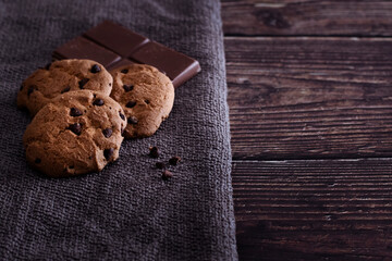 Galletas horneadas con pepitas de chocolate negro y tableta de chocolate con leche sobre una mesa de madera rústica.