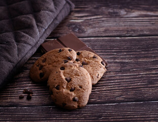 Galletas caseras con pepitas de chocolate negro y una tableta de chocolate con leche sobre una mesa de madera rústica.