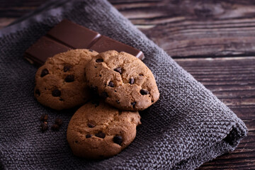 Galletas caseras con pepitas de chocolate, tableta de chocolate con leche sobre mesa de madera rústica.