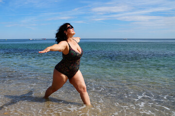 Fototapeta na wymiar lush woman performs yoga asana by the sea, warrior asana