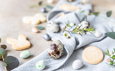 Obraz na płótnie Canvas Easter cookies with candies shaped eggs, floral decor and quail eggs on linen napkin, stone background. Holiday concept.
