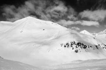 Snowy freeride trace and mountains with clouds. Black and white toned landscape.