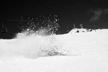 Snowboarder fall down with snow splashes on snowy ski slope. High contrast. Black and white.