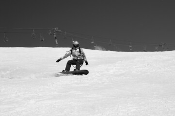 Fototapeta na wymiar Snowboarder descends on snowy ski slope at winter mountain. Black and white toned image.