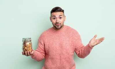 young handsome man feeling puzzled and confused and doubting. cookies bottle concept