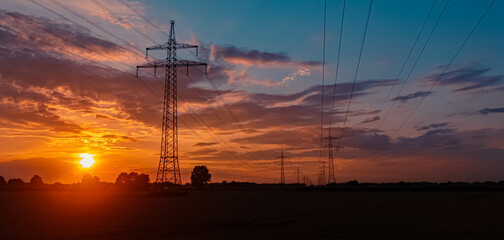 Beautiful sunset with a dramatic sky and overland high voltage lines near Tabertshausen, Bavaria, Germany