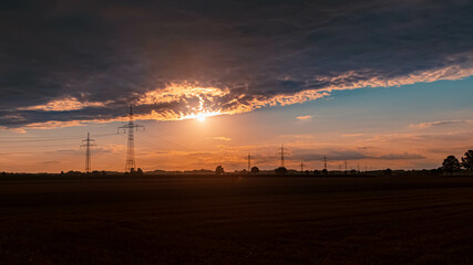 Beautiful sunset with a dramatic sky and overland high voltage lines near Tabertshausen, Bavaria, Germany