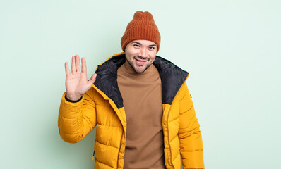 young handsome man smiling happily, waving hand, welcoming and greeting you. cold weather concept © kues1
