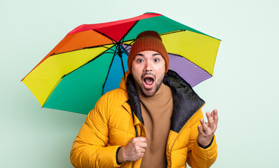 young handsome man amazed, shocked and astonished with an unbelievable surprise. rain and umbrella...