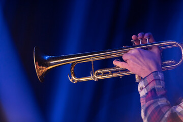 A trumpet player playing a trumpet with a checkered shirt on a blue background