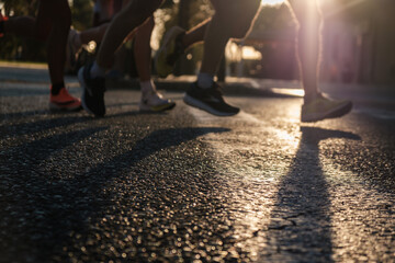 Gente corriendo una carrera de running con el sol de amanecer de fondo sobre asfalto de la ciudad