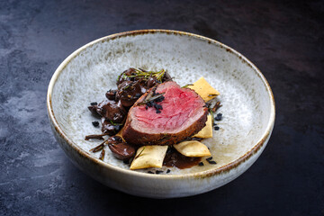 Modern Style traditionell gebratenes dry aged Angus Rinderfilet Medaillons natur mit Champignons und Cracker in Rotweinsauce serviert als close-up in einer Nordic Design Schale